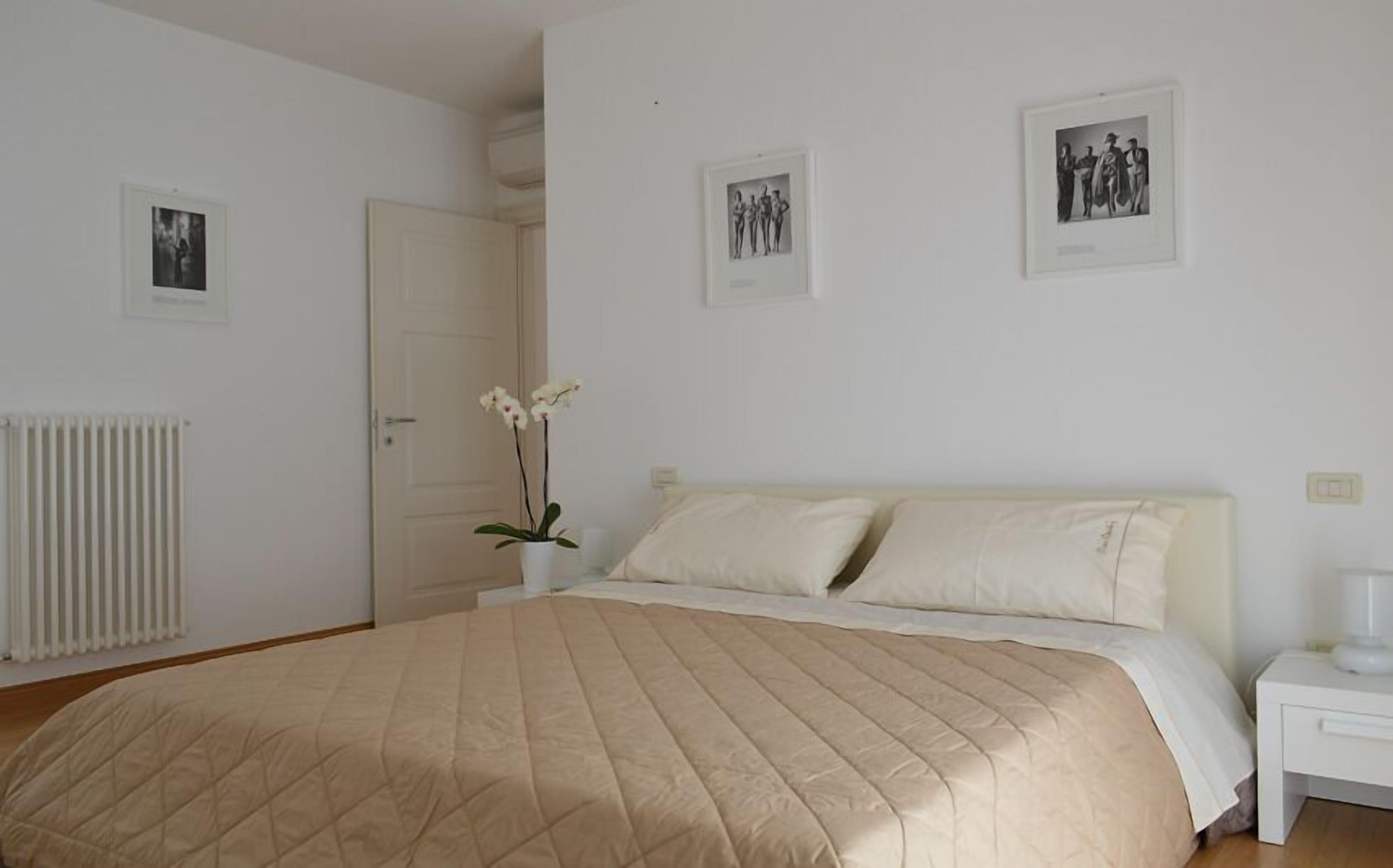 A bedroom with a large bed, white walls, and three framed pictures.