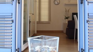 Eine geöffnete Tür, die in einen Raum führt, in dem ein Glastisch mit einer klaren Vase voller Kieselsteine steht.