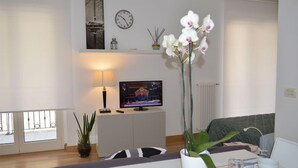 Ein Wohnzimmer mit Fernseher, einer Uhr, einer Pflanze und einem Sofa.