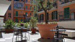 Ein Terrassenbereich im Freien mit mehreren Tischen und Stühlen, umgeben von Kübelpflanzen und einem großen Terrakottatopf.