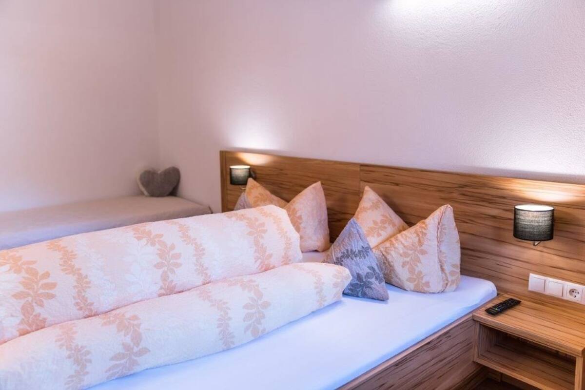 A hotel room with a wooden headboard, a bed with floral-patterned bedding, a nightstand with a lamp, and a wall-mounted light fixture.