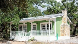 A green building with a stone chimney, white porch, and multiple windows.