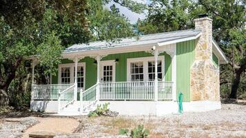 A green building with a stone chimney, white porch, and multiple windows.