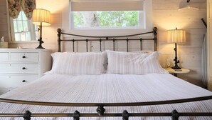 A neatly made bed with a headboard, a window above it, and two bedside lamps.