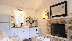 A cozy living room with a floral sofa, a stone fireplace, a white stove, and a kitchen with white cabinets and a wooden countertop.