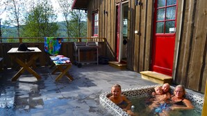 A wooden cabin with a hot tub on the deck, a picnic table, and a red door. - Fjällfrid Stugor (Bruksvallarna)