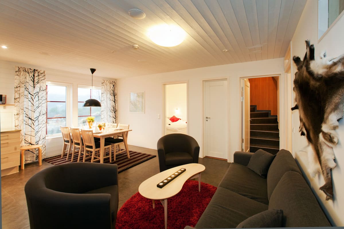 A modern living room with a sofa, chairs, a dining table, and a staircase leading to another level.