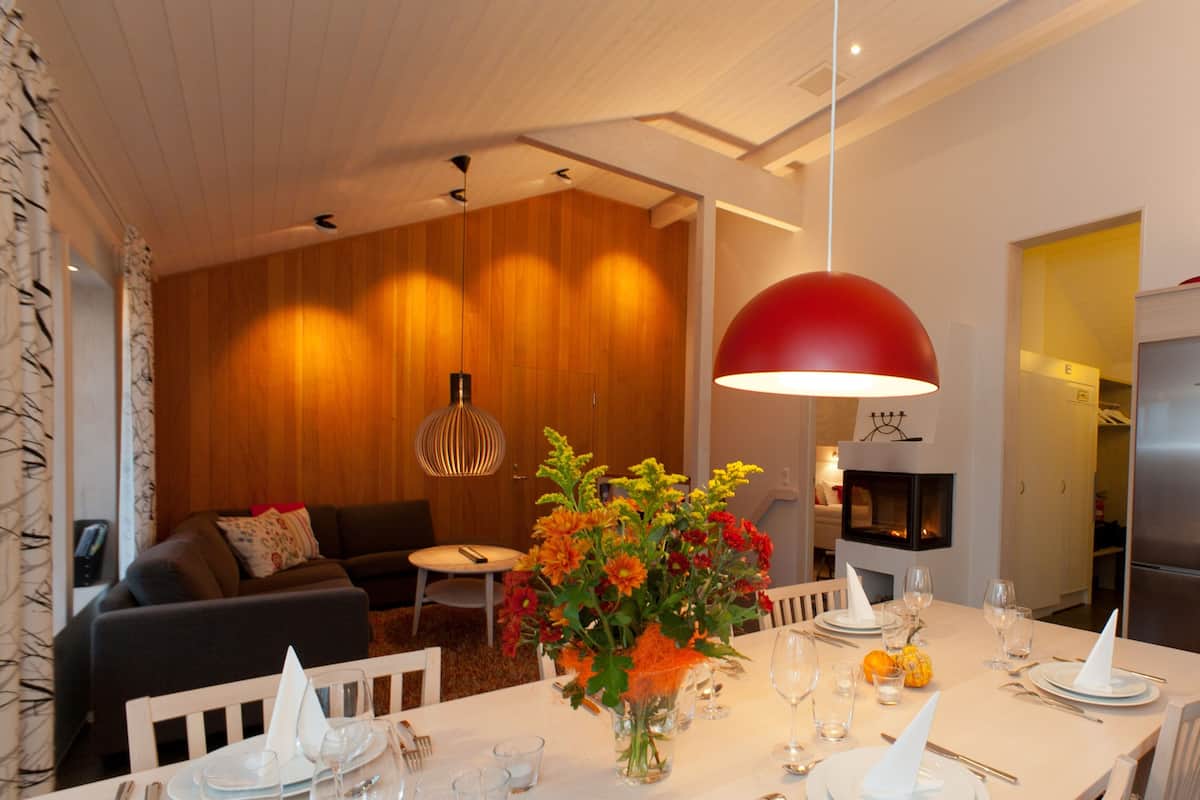 A modern dining area with a white table set for six, a vase of flowers, and a red pendant light.