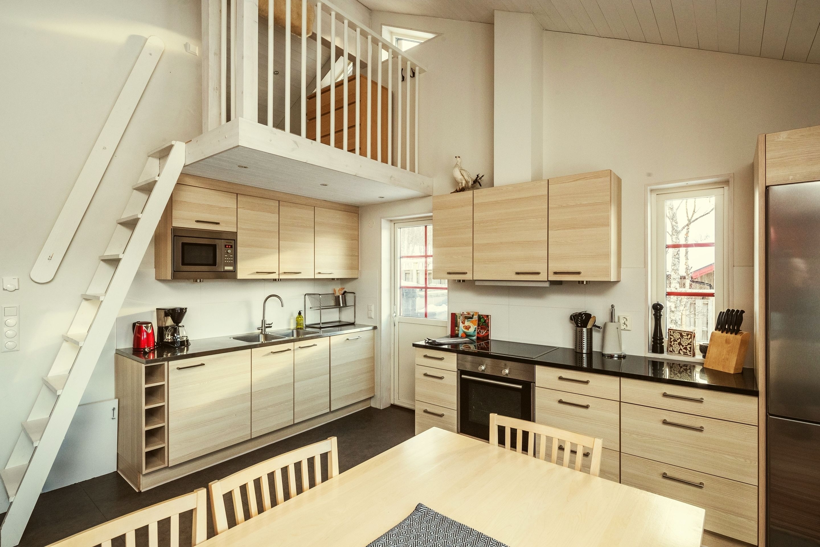 A modern kitchen with wooden cabinets, a stainless steel refrigerator, a microwave, and a dining area with a table and chairs.