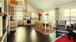 A modern kitchen with a dining area, wooden cabinets, and a loft space. - Fjällfrid Stugor (Bruksvallarna)