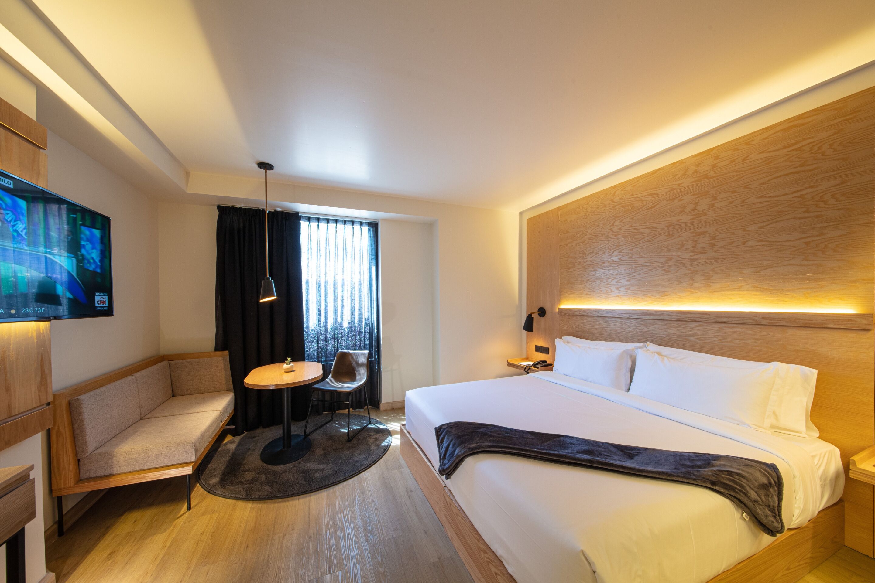 Une chambre d’hôtel moderne avec un grand lit, un canapé, une petite table et un téléviseur.