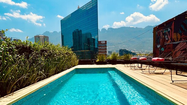 A rooftop pool with a clear view of a modern glass building and mountains in the background. - Auténtico Monterrey (San Pedro Garza García)
