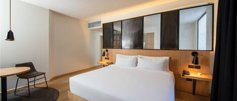 A modern hotel room with a large bed, bedside tables, a desk, and a chair.