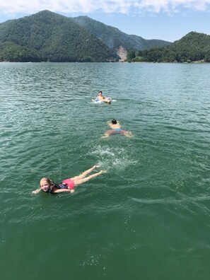 Drie mensen zwemmen in een meer, met bergen op de achtergrond.