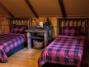 Een gezellig blokhutkamer met twee bedden, houten wanden, een klein tafeltje met een lamp en een mand.
