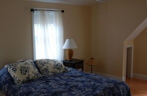 Et soveværelse med seng, natbord, lampe, et vindue med gardiner og en dør.