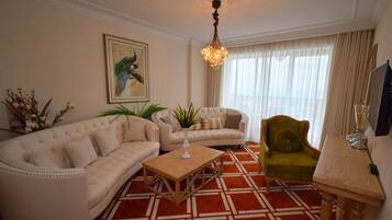 Una sala de estar con un sofá color beige, un sillón verde, una mesa de centro de madera y una araña.