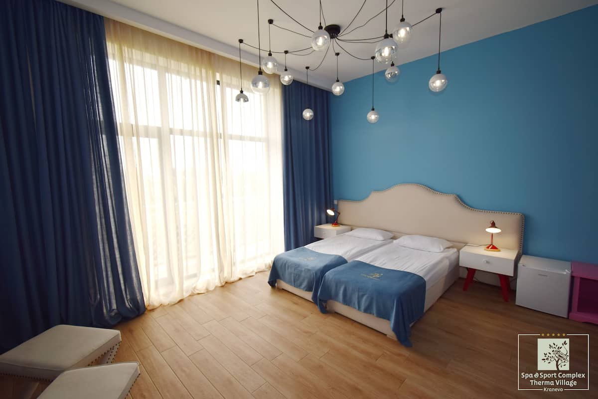 A bedroom with two beds, a nightstand with a lamp, and a window with curtains.