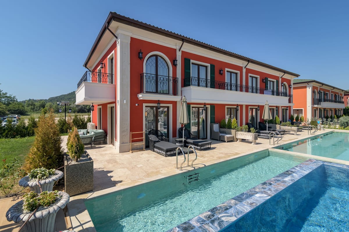 A two-story house with a swimming pool, outdoor seating, and a view of the surrounding landscape.