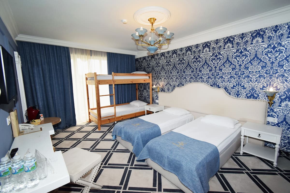 A hotel room with two single beds, a bunk bed, a desk with a telephone, and a bedside table with a lamp.