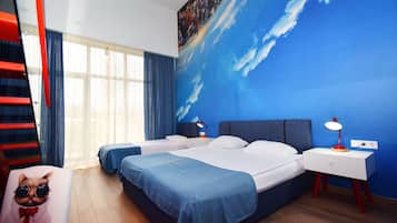 Une chambre d’hôtel avec deux lits, une fresque représentant un ciel bleu, une lampe rouge et blanche, et un fauteuil à motifs félins.