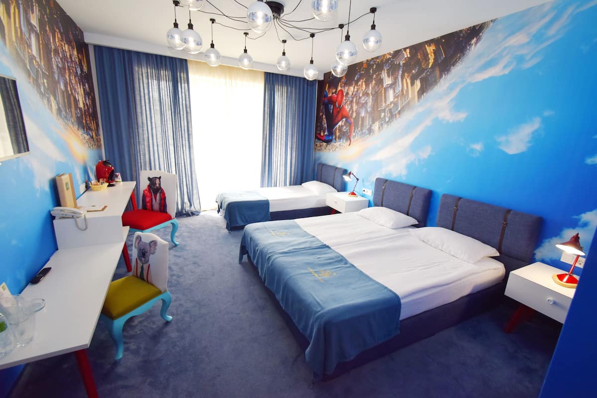 A hotel room with two beds, a desk, a chair, and a large mural on the wall.