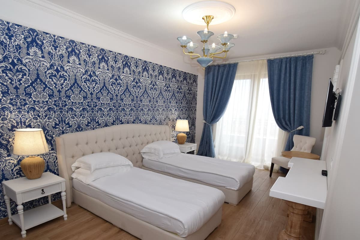 A bedroom with two beds, a white headboard, a nightstand with a lamp, and a blue patterned wall.