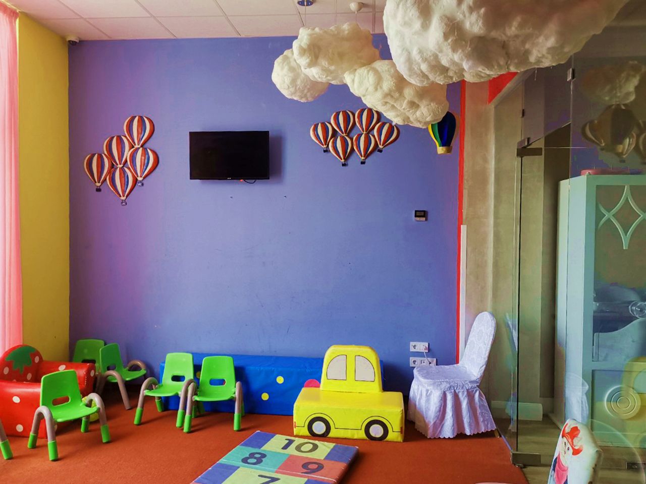A children's playroom with colorful chairs, a play mat, and a toy car.