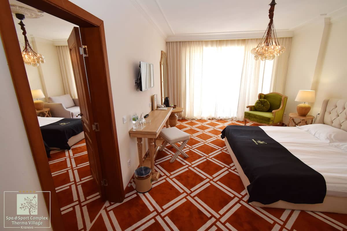 A hotel room with two beds, a desk, a chair, a mirror, a lamp, and a window with curtains.