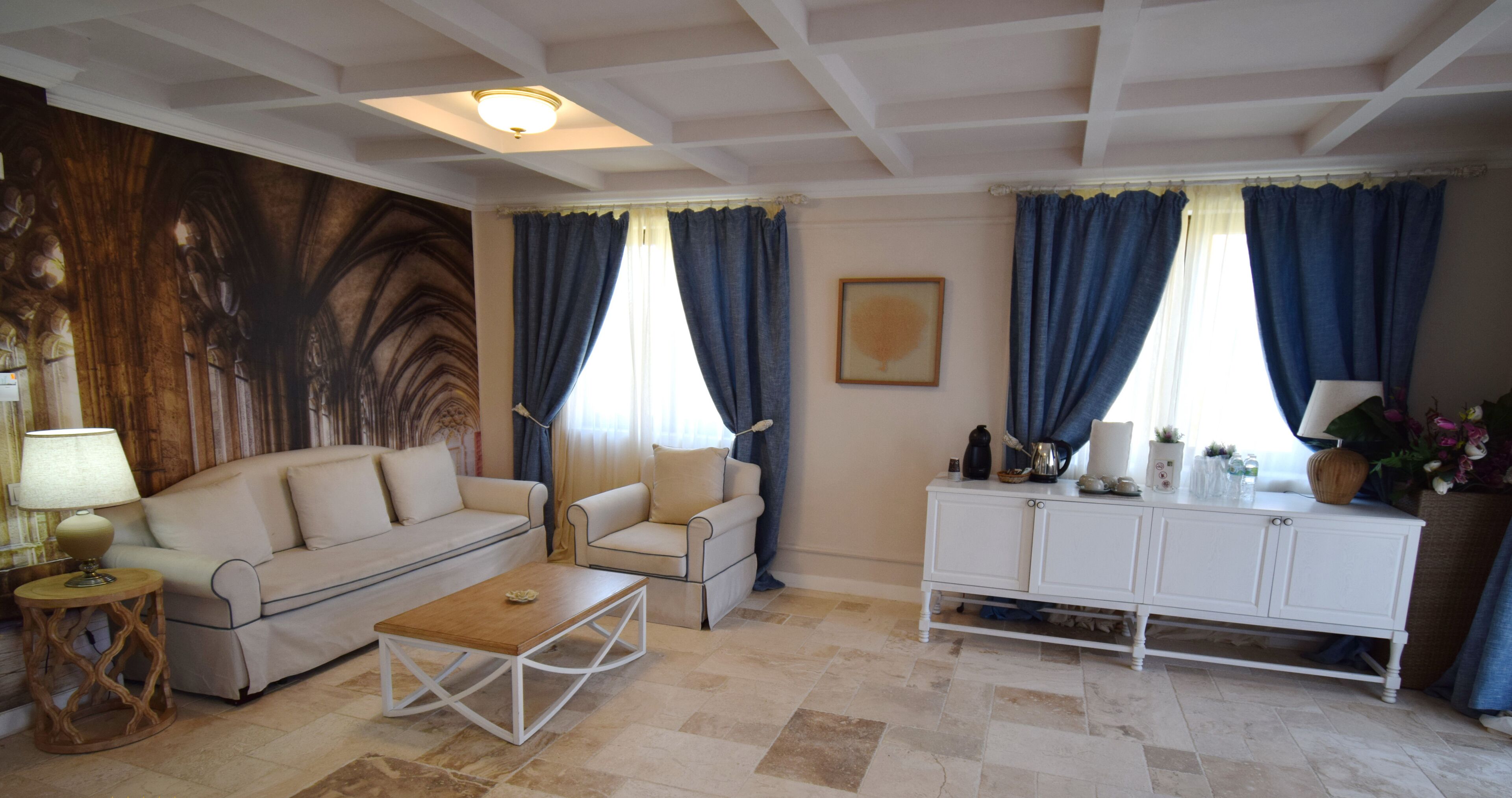 Una sala de estar con un sofá color crema, una mesa de centro de madera, un armario blanco y un mural grande en la pared.
