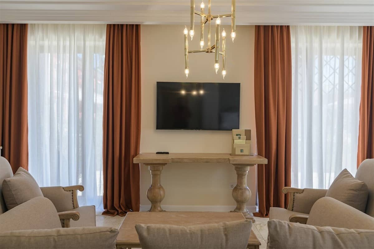 A living room with a flat-screen TV mounted on the wall, a wooden console table, and a chandelier.