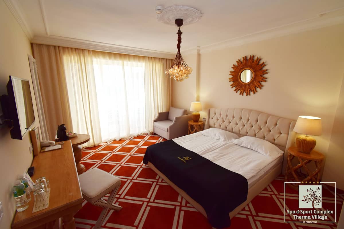 A hotel room with a large bed, a desk, a chair, a TV, and a window with curtains.
