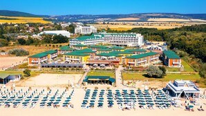 Ett hotell med flera byggnader, ett strandområde med många parasoller och utsikt över det omgivande landskapet.
