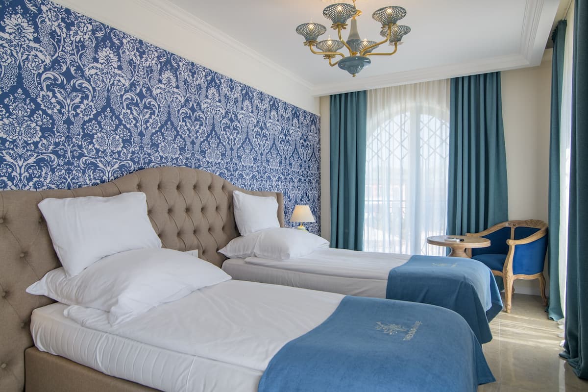 A hotel room with two beds, a chandelier, a small round table, and a chair.