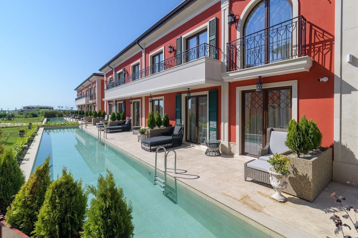A large, modern hotel with a swimming pool, outdoor seating, and a red facade.