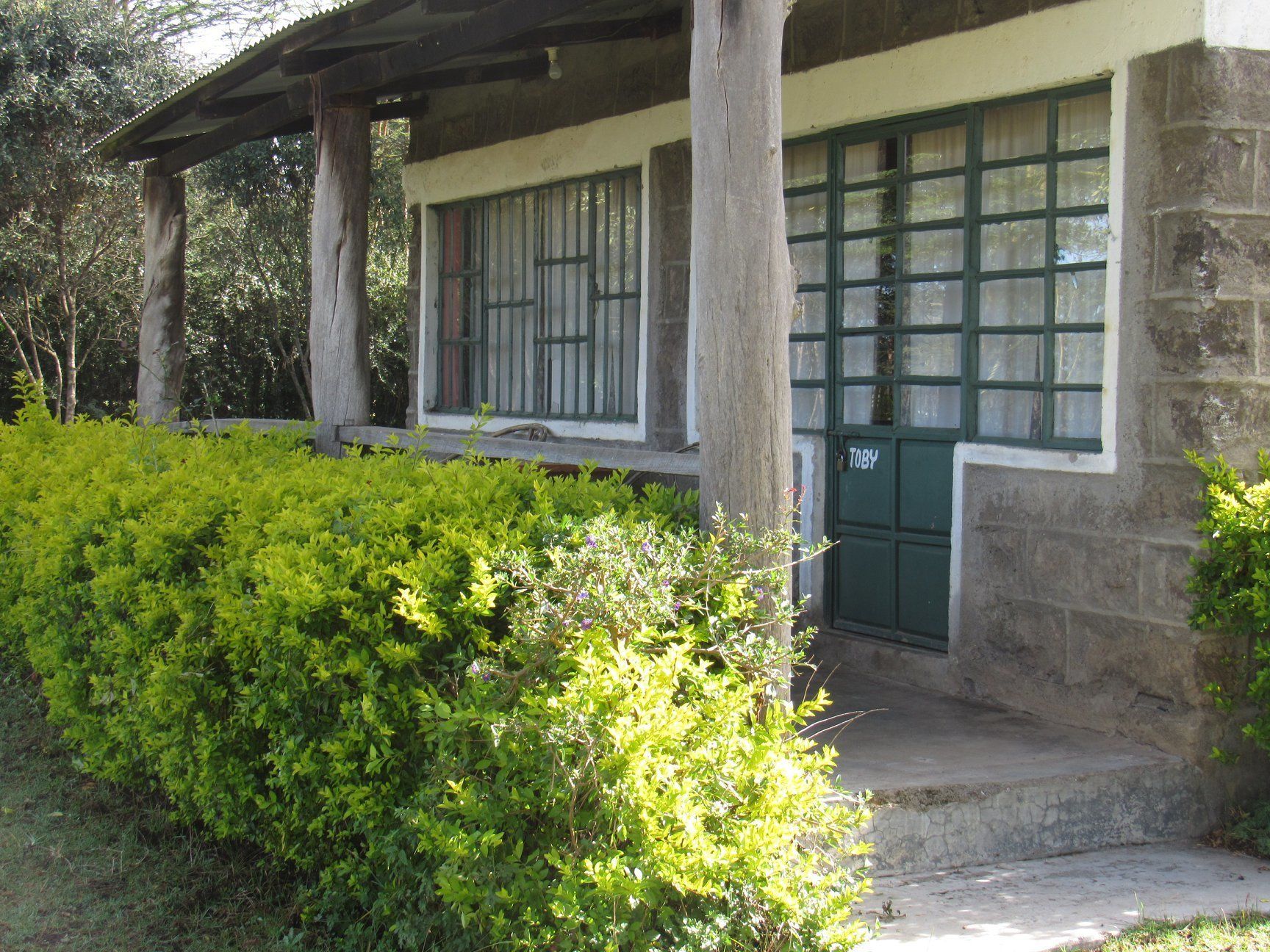 Un edificio de piedra con puerta verde y ventanas, rodeado de abundante vegetación.
