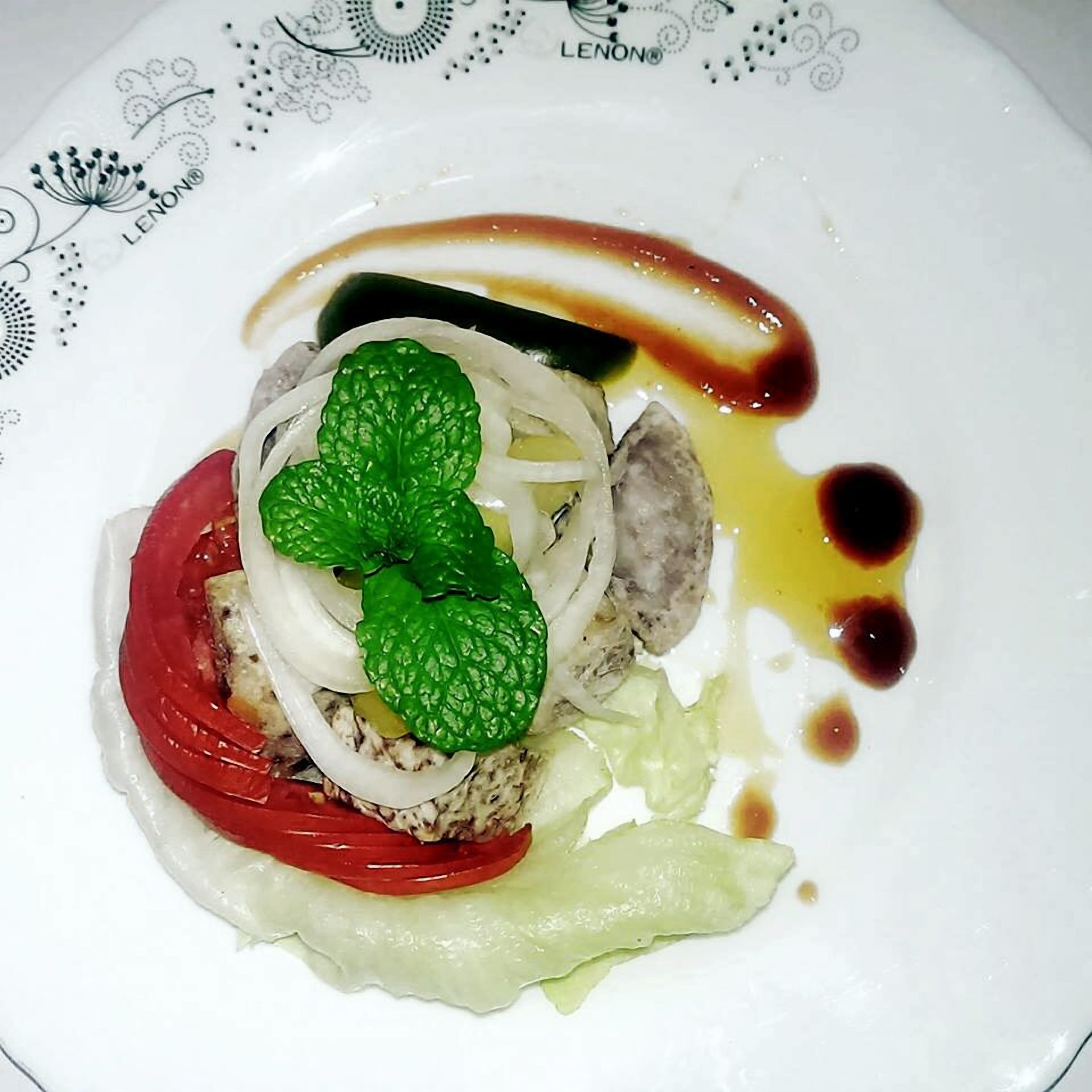Un plato con un alimento, posiblemente una tarta o un pastel, cubierto con una hoja verde, fruta roja y láminas de cebolla blanca.