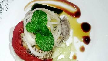 Un plato con un alimento, posiblemente una tarta o un pastel, cubierto con una hoja verde, fruta roja y láminas de cebolla blanca.
