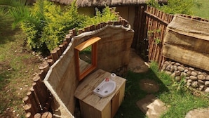 A rustic outdoor bathroom with a wooden bench, a small sink, and a mirror.