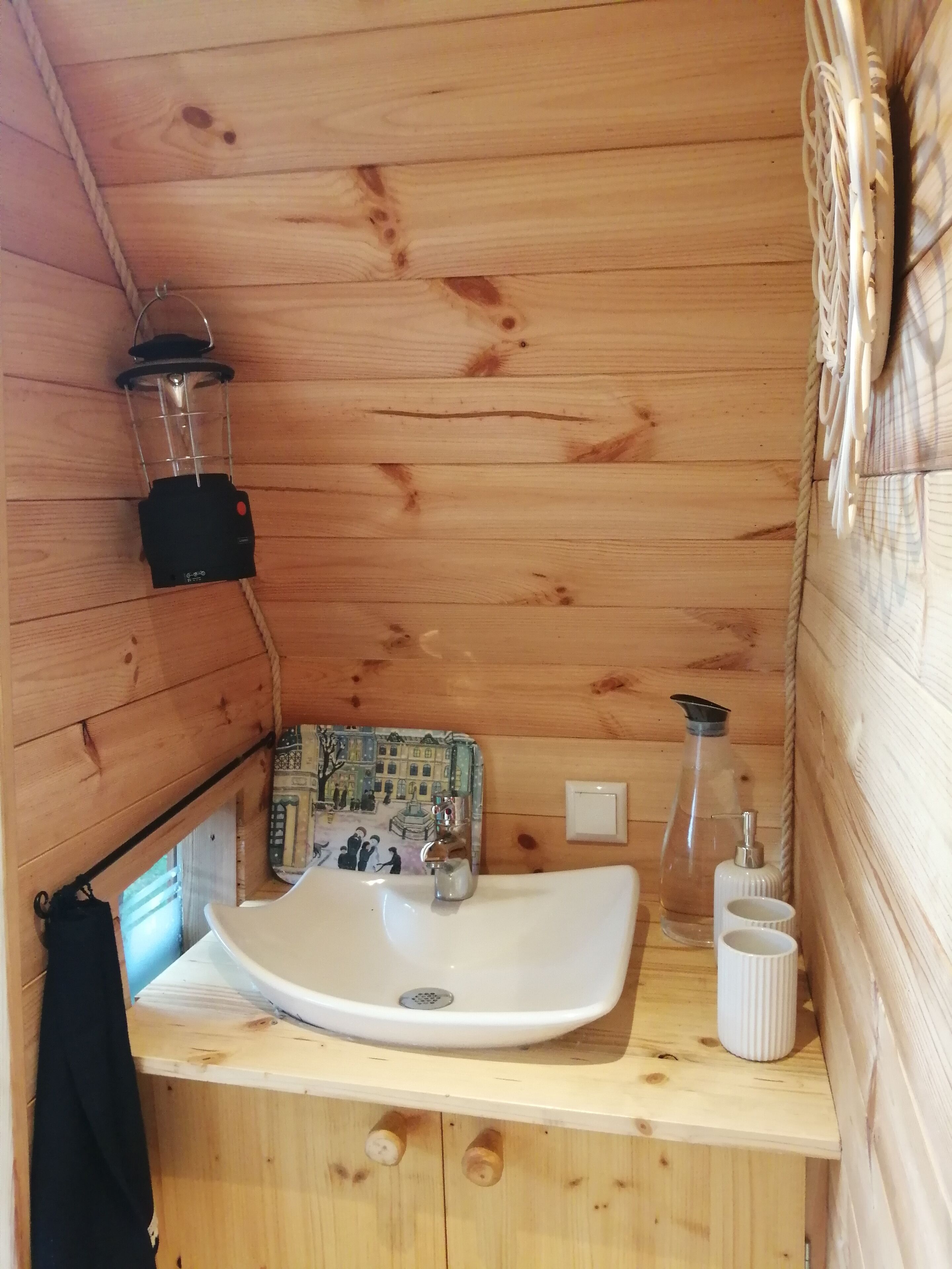 Une salle de bain rustique, avec des murs en bois, un lavabo blanc, une lanterne suspendue et un petit miroir.