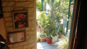 A stone wall with a framed picture of flowers and a plaque. Outside, there are potted plants and a view of a garden through a glass door. - Le Frêne Fringant (Sainte-Opportune-la-Mare)
