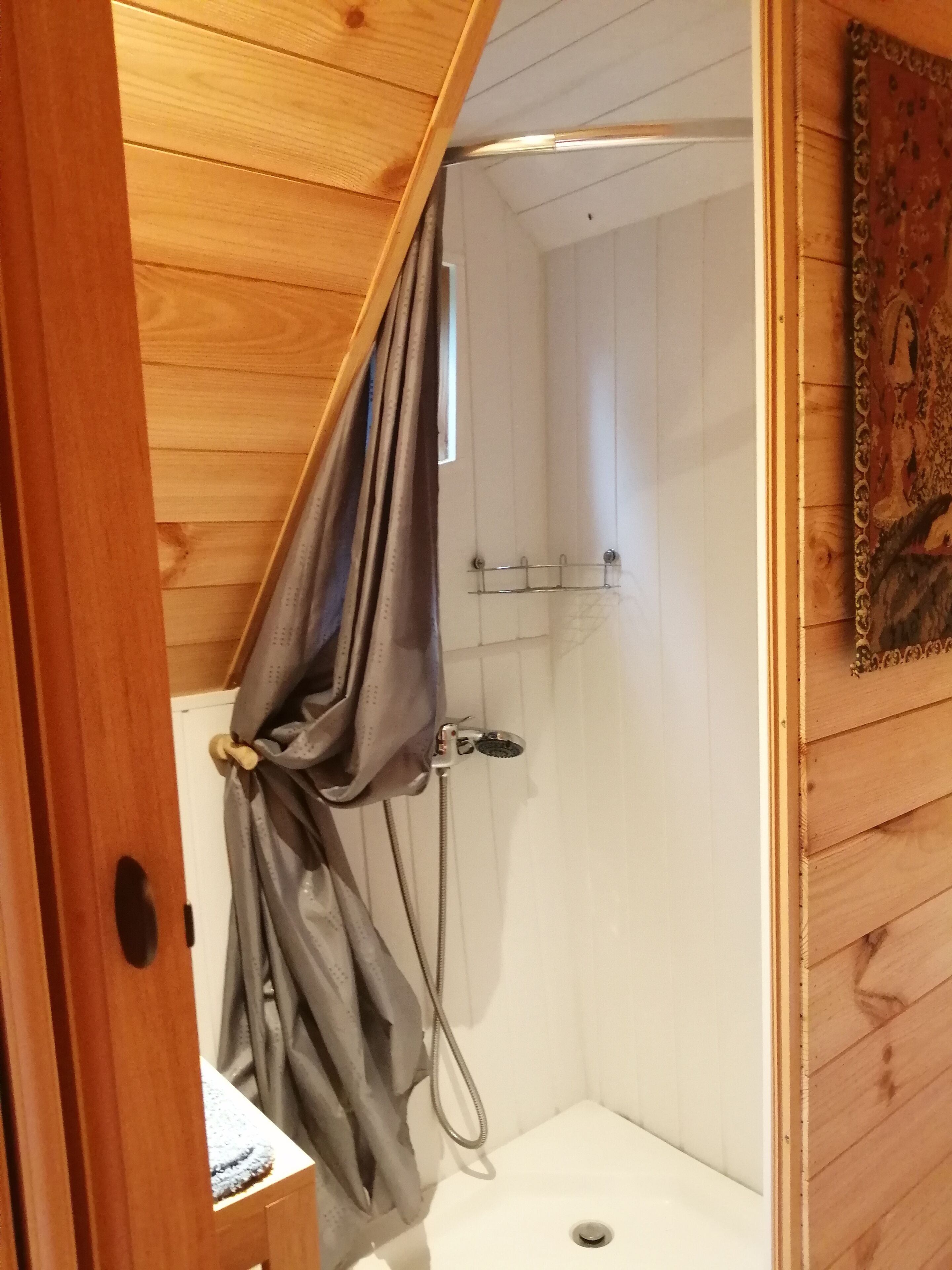 A wooden-paneled bathroom with a shower, a towel rack, and a small sink.