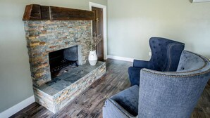 A living room with a stone fireplace, a blue armchair, and a vase with dried branches. - Wine Suite at Rellik House. Winery & Alpaca Farm (Central Point)