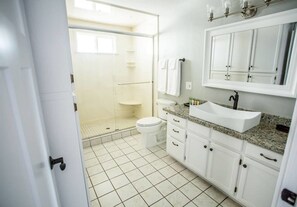 A bathroom with a shower, toilet, sink, and cabinets.