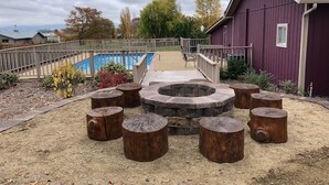 A circular seating area with a fire pit in the center, surrounded by eight wooden stools. - Alpaca Suite at Rellik House. Winery & Alpaca Farm (Central Point)