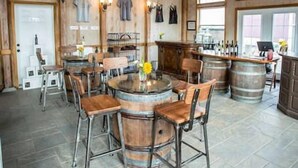 A rustic interior with a high wooden ceiling, stone flooring, a central round table with chairs, and a bar area with barrels. - Raven Suite at Rellik House. Winery & Alpaca Farm (Central Point)