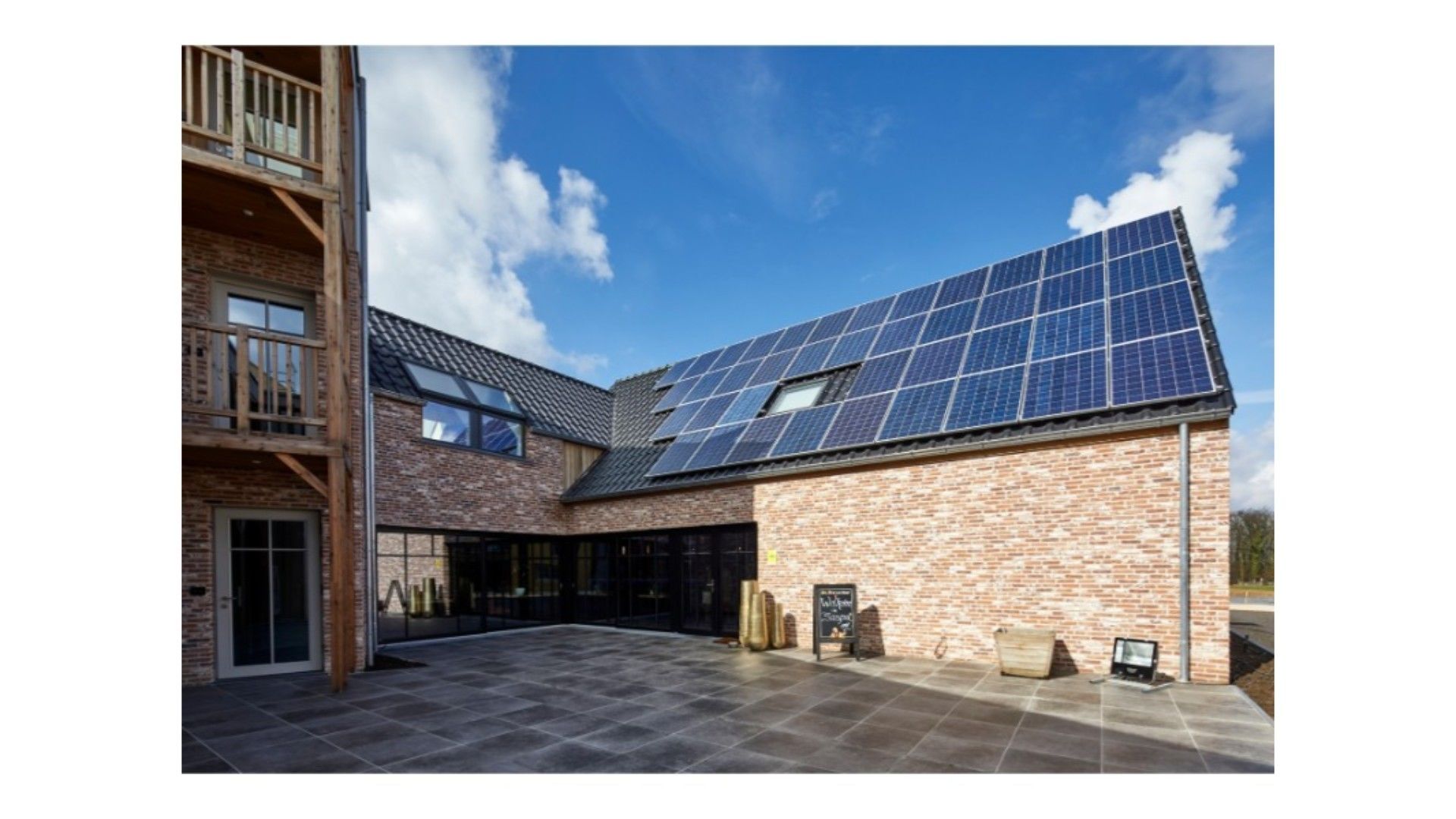 Ein Gebäude mit Ziegelaußenwand, einer großen Solaranlage auf dem Dach und einem überdachten Außenbereich mit Fliesenboden.