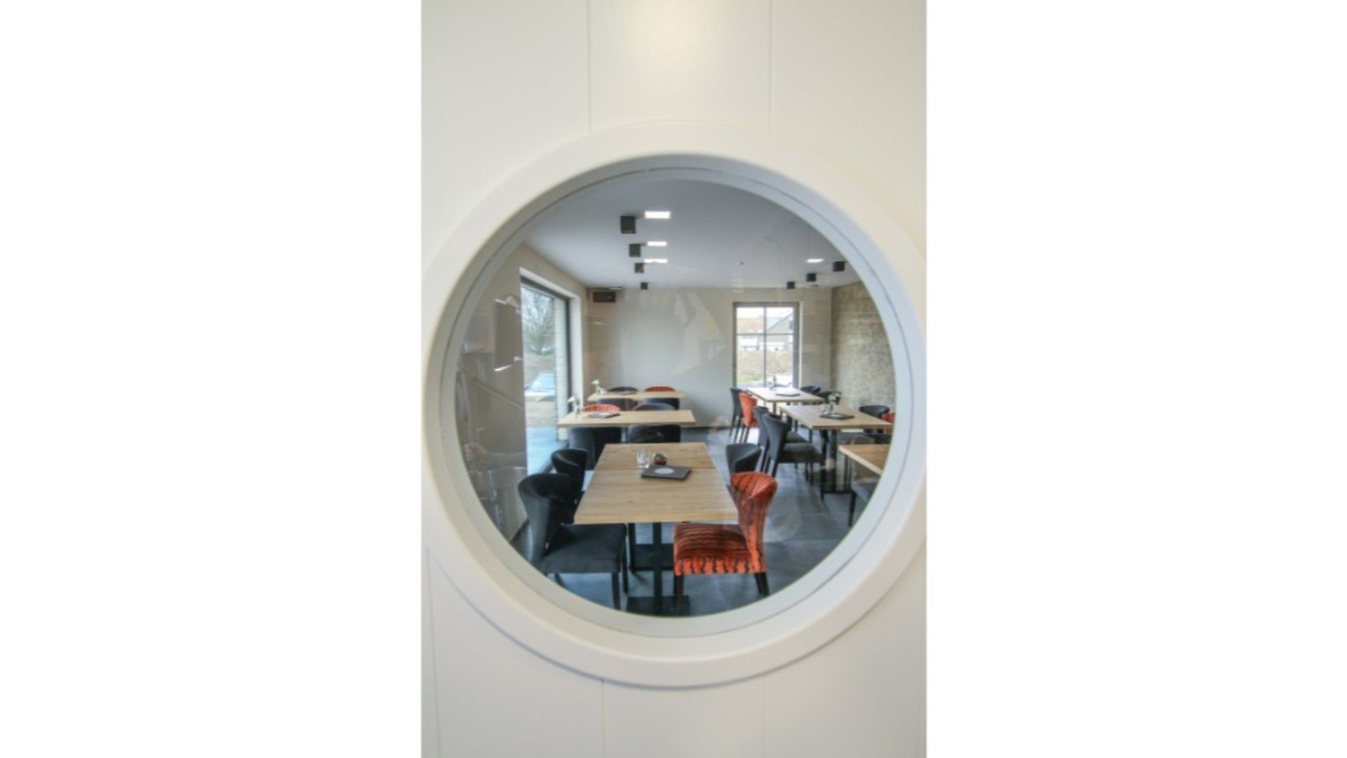 A dining area with round tables and chairs, large windows, and a circular window frame.