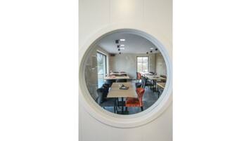 A dining area with round tables and chairs, large windows, and a circular window frame.