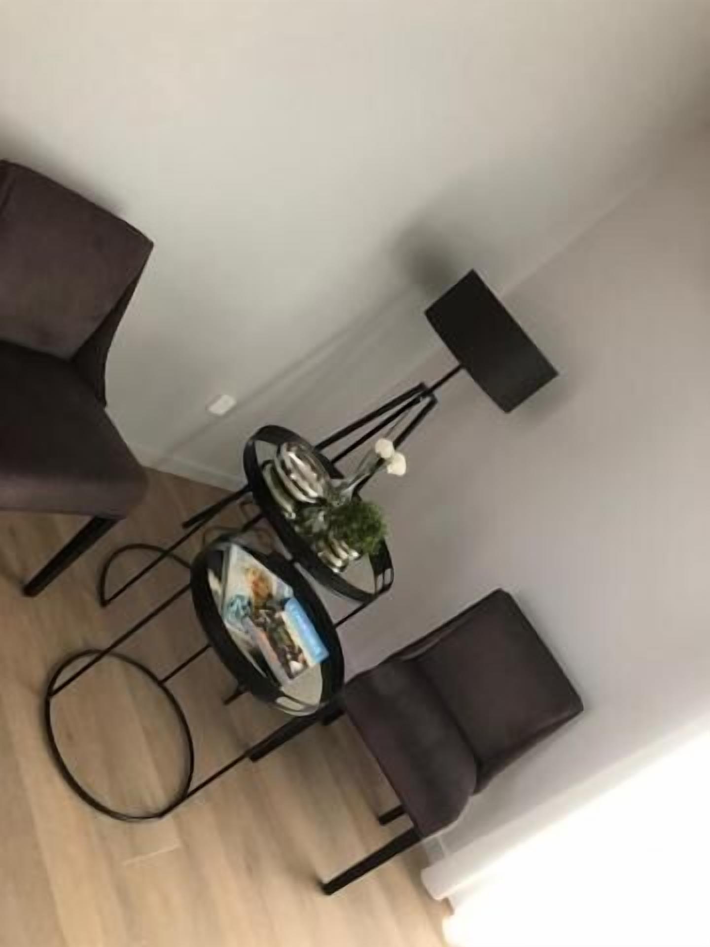 A room with a dark brown armchair, a small round table with a magazine, a lamp, and a chair.